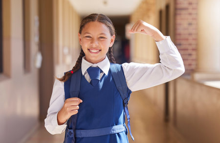 Education, school and student flexing arm for girl power, growth and development with a backpack with books. Smile, scholarship and happy child excited about learning, knowledge and future successの写真素材