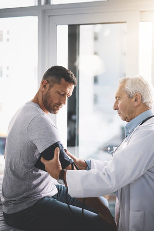 Let me just get your blood pressure. a senior doctor giving his male patient a thorough checkup during his consultation.の写真素材