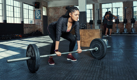 Shes working towards her fitness goals. a young woman lifting weights in a gym.の写真素材