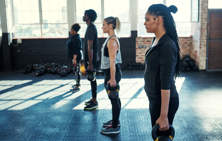 Nothing can stop us. a focused group of young people standing in a row and training with weights in a gym.の写真素材