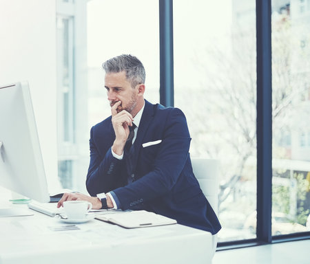 The hard work that goes into career success. a mature businessman using a computer at his desk in a modern office.の写真素材