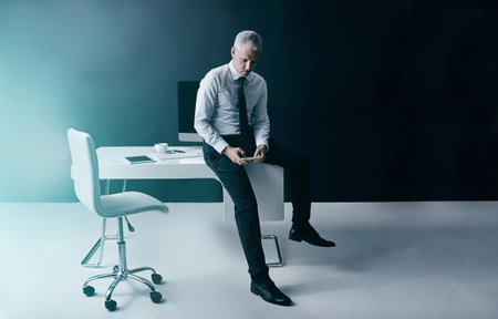 Business at the touch of a button. a focussed businessman using his smartphone while sitting on his desk in the office.の写真素材