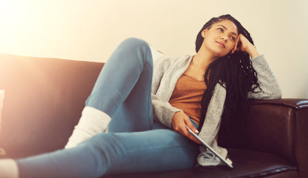 Lets see how long I can survive without my series...a young woman contemplating while relaxing at home with her tablet.の写真素材