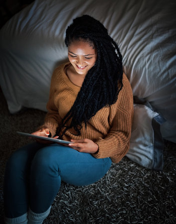 Last social media post for the day. a relaxed young woman using a digital tablet during the evening at home.の写真素材