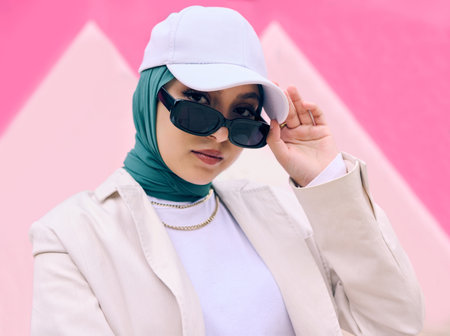 Muslim woman, fashion and sunglasses in portrait by wall, gen z aesthetic or beauty with art deco in city. Young islamic girl, student and clothes with pride, freedom or cap for travel in Dubai metroの写真素材