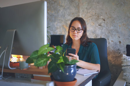 Making sure the data is right. an attractive young woman sitting alone and using her cellphone while working from home.の写真素材