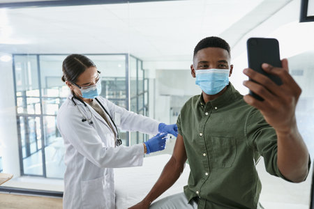 Recording this memorable moment. a young doctor giving a patient an injection while he takes a selfie in an office.の写真素材