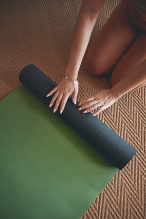 Its not just a mat, its my magic carpet. High angle shot of an unrecognisable woman rolling a yoga mat while exercising at home.の写真素材