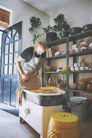 Cleaning as you go is the way to go. a young man cleaning a pottery wheel in a ceramic studio.