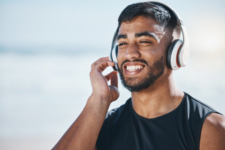 Happy, beach and a man with music for fitness, running motivation and ideas in nature. Smile, wellness and an athlete listening or streaming a podcast while training or exercise vision at the seaの写真素材