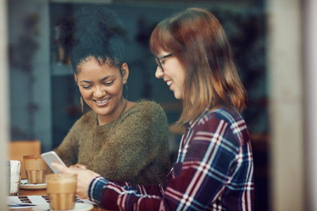 This is the app I was telling you about...two young friends looking at something on a cellphone in a cafe.の写真素材