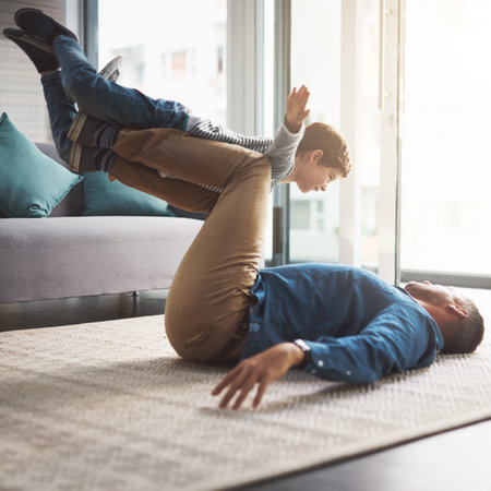 Im flying. a cheerful little boy playing around and being lifted by his dad with his legs in the living room at home during the day.の写真素材