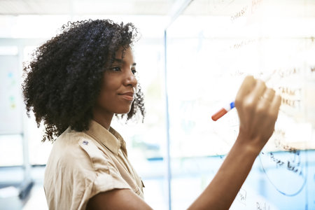Every idea gets her closer to the success she seeks. a young businesswoman writing notes on a glass screen in an office.の写真素材