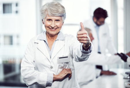 Heres too making the world a better and safer place. Portrait of a cheerful elderly female scientist showing thumbs up while looking into the camera inside a laboratory.の写真素材