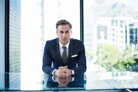 I know what I bring to the table. portrait of a successful businessman sitting at his desk in an office.の写真素材