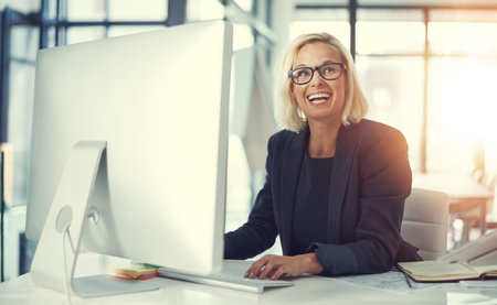 Thats a brilliant idea. a happy businesswoman using a computer at her work desk.の写真素材