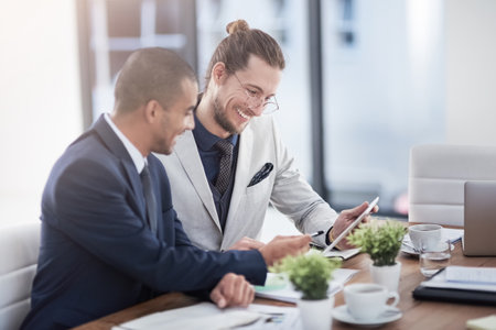Modern technology makes marketing your business so much simpler. two young businessmen using a digital tablet together at work.の写真素材