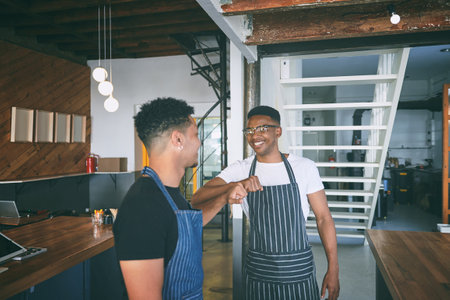Buddies in life and in business. two confident young men giving each other a fist bump while working in a cafe.の写真素材