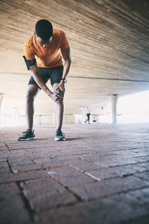 The harder I run the more it hurts. a young man experiencing joint pain while working out against an urban background.の素材 [FY310206508537]