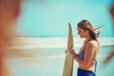 Time to hit the water. a beautiful young woman going for a surf at the beach.の写真素材