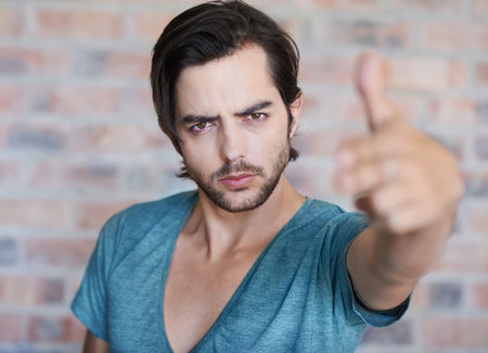 Rebel without a cause. Portrait of a good looking man against a brick wall making a gesture with his hand.の写真素材