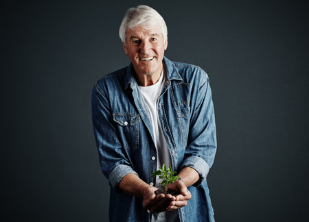 Nature needs to be nurtured. Studio portrait of a handsome mature man holding a budding plant against a dark background.の写真素材