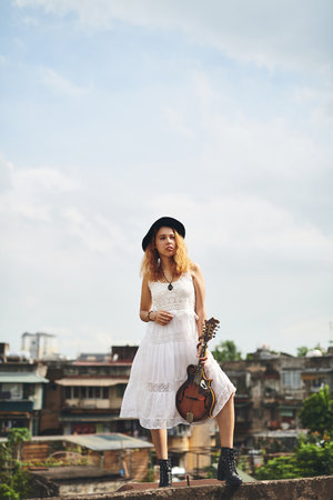 My guitar goes wherever I go. a young woman out on a rooftop with her guitar.の写真素材