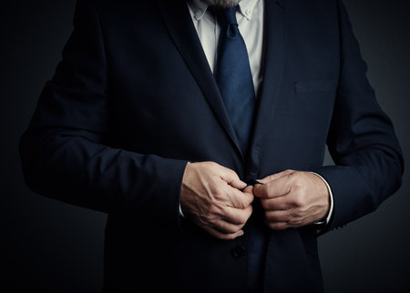 Wear your suit with pride. Studio shot of an unrecognizable mature businessman buttoning his jacket while standing against a dark background.の写真素材