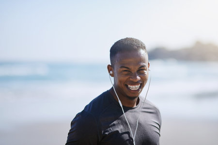 Morning jogs on the beach are my thing. Portrait of a sporty young man listening to music while exercising outdoors.の写真素材