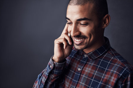 Fill me in on the details. Studio shot of a young man talking on a cellphone against a dark background.の写真素材