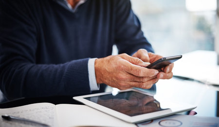 Hes connected and kept up to date. a businessman using a mobile phone at his work desk.