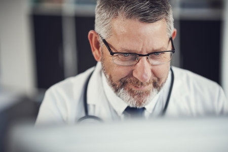 Making quicker diagnoses with modern technology. a mature doctor using a computer at a desk in his...