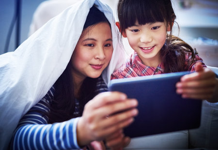 Youve gotta make time for family. an attractive young woman and her daughter using a digital tablet while lying under the covers.の写真素材
