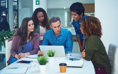 Using online tools for a better outcome. a group of designers gathering around a man using a laptop...