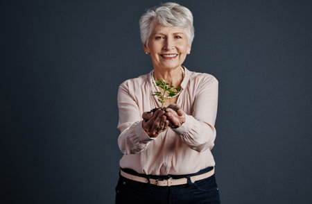 Just like humans, plants grow more beautiful with age. Studio shot of a cheerful elderly woman standing with a plant in her hands while looking into the camera.の写真素材