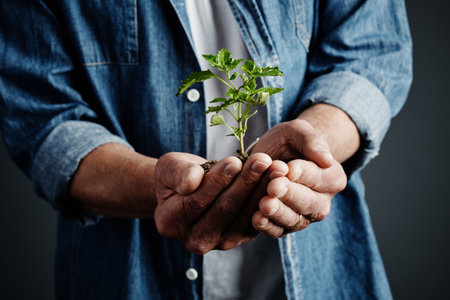 Gentle hands. Studio shot of an unrecognizable man holding a budding plant against a dark background.の写真素材