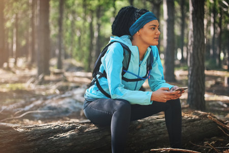 Strive for progress, not perfection. an athletic young woman sending a text while jogging in the woods.の写真素材