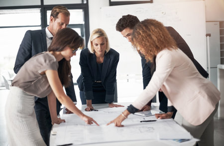 Efficient planning is a team effort. a team of professionals working on blueprints in an office.