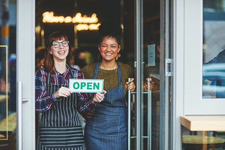 Come and visit our new brand new store. two young women holding up an open sign in their coffee...