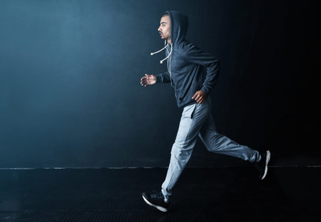 Hes on his way. Studio shot of a sporty young man running against a dark background.