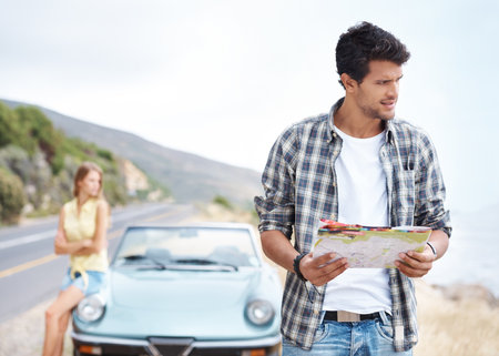I think we took a wrong turn somewhere...Handsome young guy trying to find his way on a roadtrip while his girlfriend looks on in annoyance.の写真素材