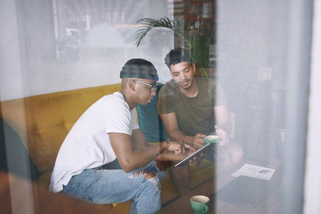 Discussing business at our favourite cafe. two young men discussing something on a digital tablet while having coffee together.の写真素材