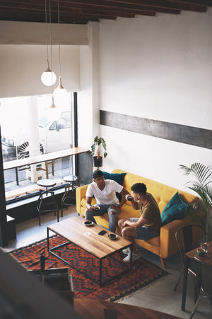 The best stories are shared over coffee. two young men sitting together in a coffee shop.の写真素材