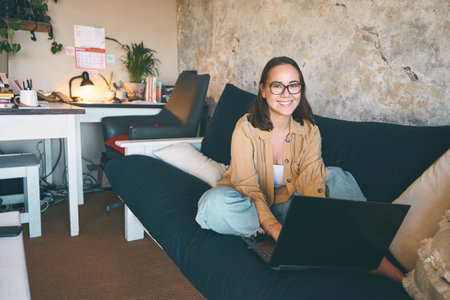 In my own space, living life at my own pace. a young woman using a laptop on the sofa at home.の写真素材