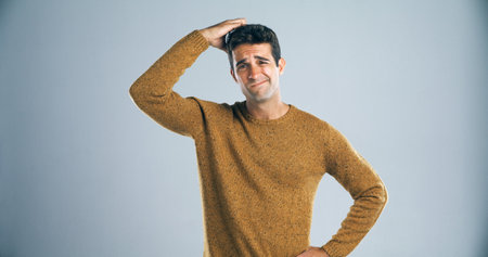 I have no idea what Im doing. Studio shot of a handsome young man scratching his head in confusion against a gray background.の写真素材