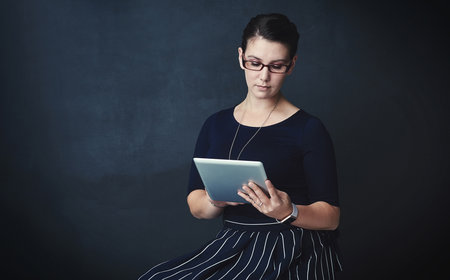 Reading up on the latest in corporate trends. Studio portrait of a corporate businesswoman using a digital tablet against a dark background.の写真素材