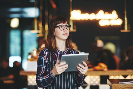 Keeping her cafes social media account fresh with daily updates. a young woman using a digital tablet while working at a coffee shop.の写真素材