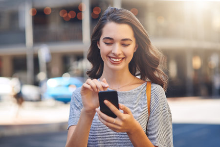 Hooking up with friends in the city. an attractive young woman sending text messages while spending her day out in the city.の写真素材
