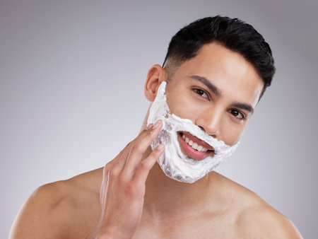 Happy, shaving and foam with portrait of man in studio for hair removal, grooming and skincare. Cosmetics, self care and morning with face of male model on gray background for cleaning and productの写真素材