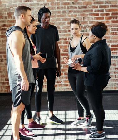 Everyone still okay. a cheerful young group of people standing in a circle and having a conversation before a workout in a gym.の写真素材